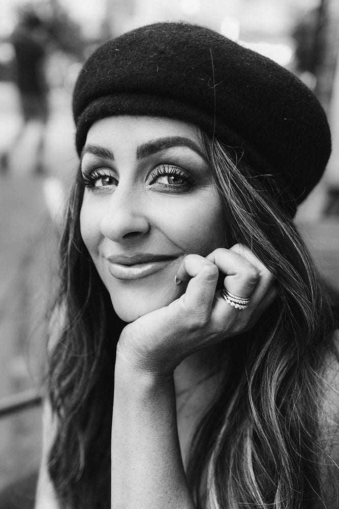 Black and white portrait of a smiling woman in a beret, chin resting on her hand