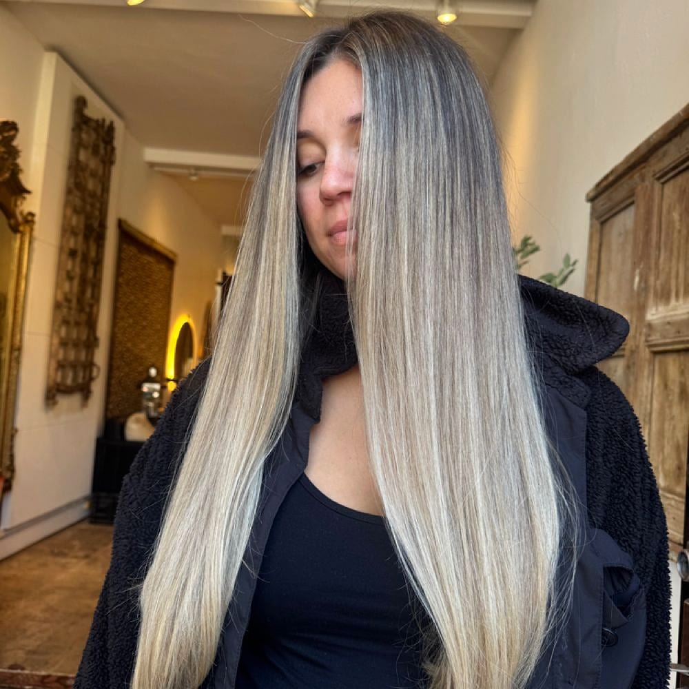 Long straight blonde and grey balayage, the client looking down in a salon hallway